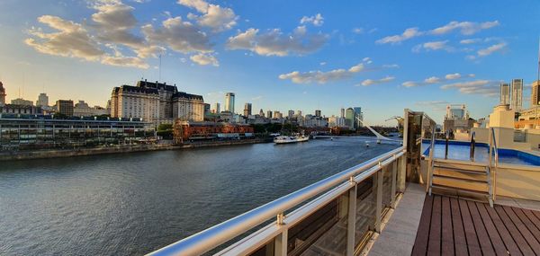 Bridge over river by buildings in city against sky