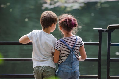 Rear view of siblings standing by railing against lake