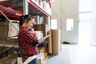 Determined female manual worker wearing headphones while using digital tablet at warehouse