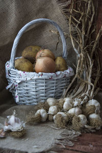 Close-up of potatoes and onions in basket by garlics on table