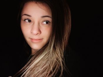 Close-up portrait of a smiling young woman over black background