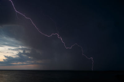 Forked lightning over sea against sky at night