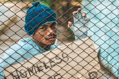 Portrait of young man looking through chainlink fence