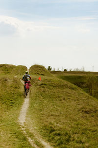 Rear view of people riding bicycle on field