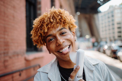 A young man with curly hair is holding a cup of coffee and smiling
