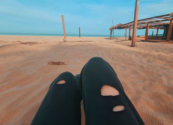 Low section of person relaxing on sand at beach against sky