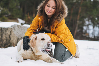 Young smiling woman in yellow jacket with big kind white dog labrador walking in winter forest