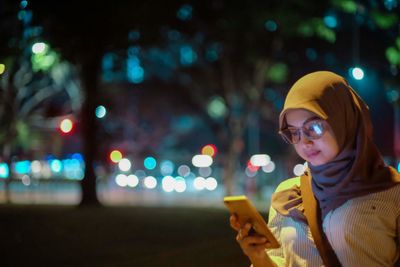 Woman wearing hijab using phone outdoors at night