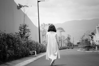 A young girl wearing a dress walking on the street away from the camera 