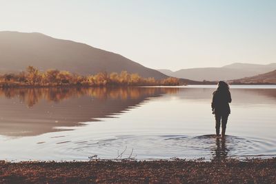 Rear view of man standing by lake against sky
