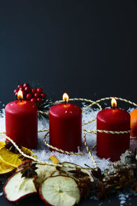 Close-up of burning candles and decorations during christmas against black background