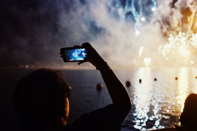 Rear view of person photographing through smart phone at fireworks