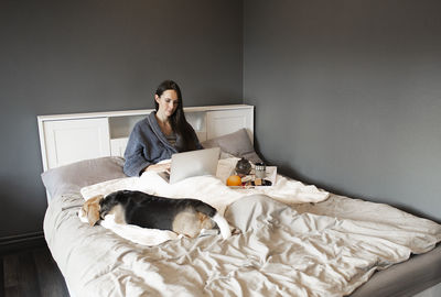 Woman girl and dog is enjoying tea and breakfast in the bed. working on the laptop.video chat.