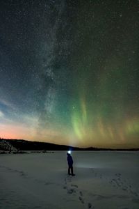 Rear view of man standing on field against sky at night