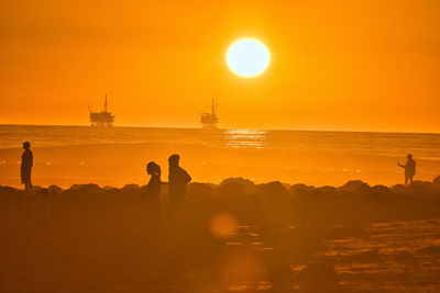 Silhouette people on beach against orange sky