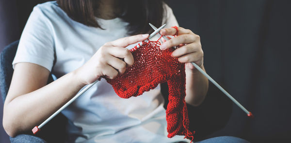 Midsection of woman knitting wool while sitting at home