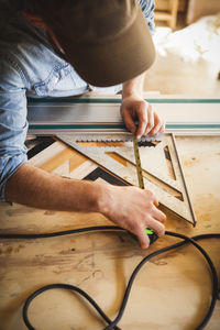 Cropped image of artist using metallic tape measure while working on wooden art at workshop