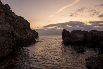 Rocks in sea against sky during sunset