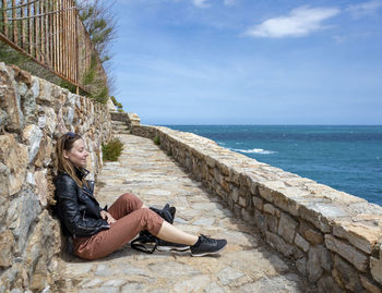 Man sitting on rock by sea against sky