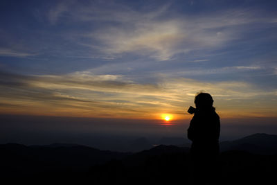 Silhouette woman standing on mountain against sky during sunset