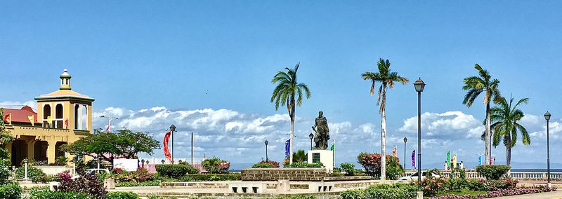 Panoramic view of palm trees and buildings against blue sky