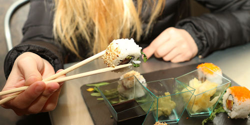 Cropped image of woman eating sushi at restaurant