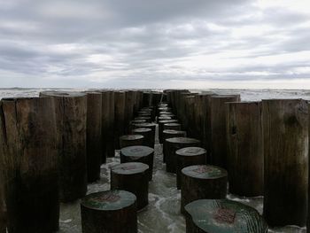 Wooden posts amidst sea against sky