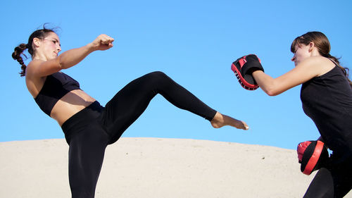 Two athletic, young women in black fitness suits are engaged in a pair work out kicks train to fight