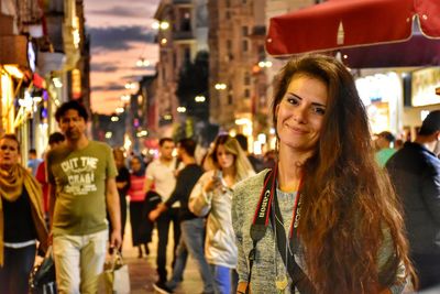 Portrait of young woman on illuminated street in city at night