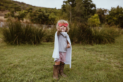 Blond boy wearing cape gesturing while standing on meadow