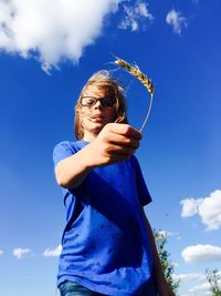 Low angle view of boy holding wheat plant against blue sky