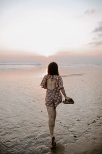 Rear view of woman standing at beach against sky during sunset