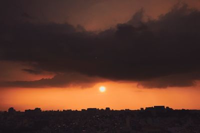 Silhouette buildings against dramatic sky during sunset
