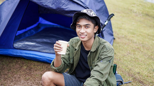 Portrait of young man holding drink while camping outdoors