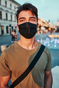 Young man standing in the city center in the evening, looking away, wearing the face mask