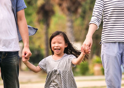 Cheerful daughter holding parents hands while walking at park