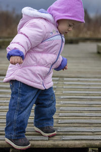 Cute baby girl wearing warm clothing standing on footpath