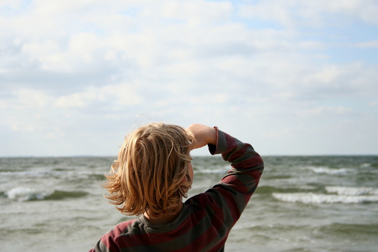 sea, leisure activity, horizon over water, lifestyles, rear view, sky, water, headshot, cloud - sky, holding, beauty in nature, non-urban scene, scenics, wave, tranquility, enjoyment, nature, tourism, casual clothing, focus on foreground, tranquil scene, travel destinations, vacations, long hair, wind, person, day