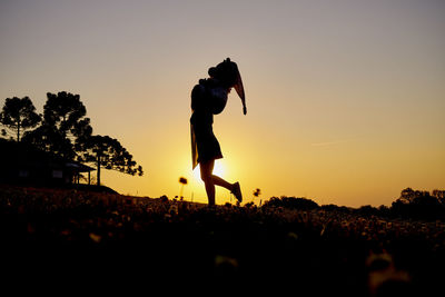 Silhouette woman walking on field against sky during sunset