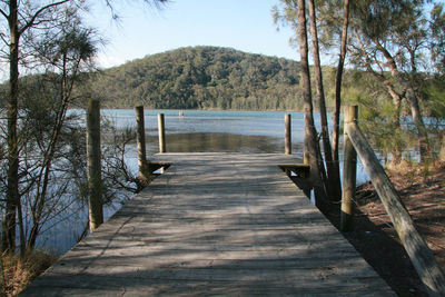 Wooden footbridge by lake against sky