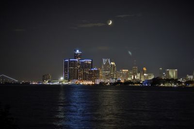 Illuminated city by sea against sky at night