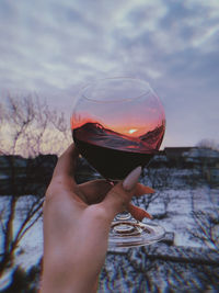 Close-up of hand holding glass of drink against sky