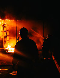 Rear view of silhouette man standing against illuminated fire at night