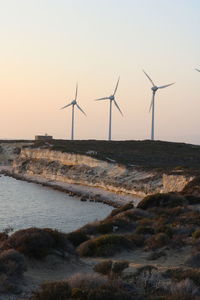 Wind turbines on land against sky during sunset