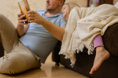 Dad entertains the child during illness. he looks, reads a book, a photo book with his daughter home