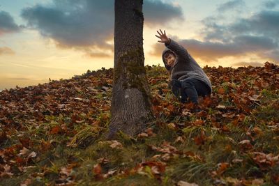 Man sitting on field by tree against sky during sunset