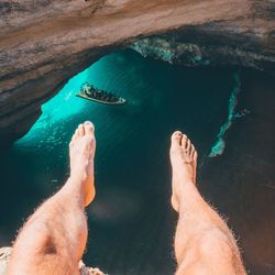 Low section of man sitting on cliff above sea