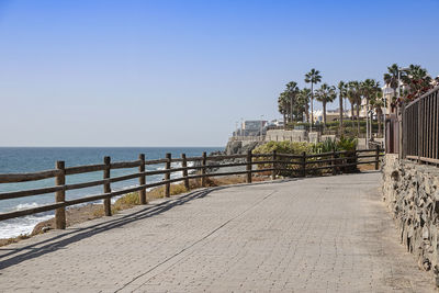 Footpath by sea against clear sky