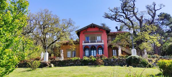 House and trees by plants against sky