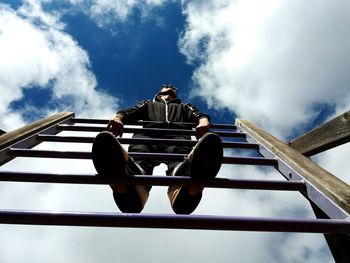 Directly below shot of man standing on ladder against cloudy blue sky